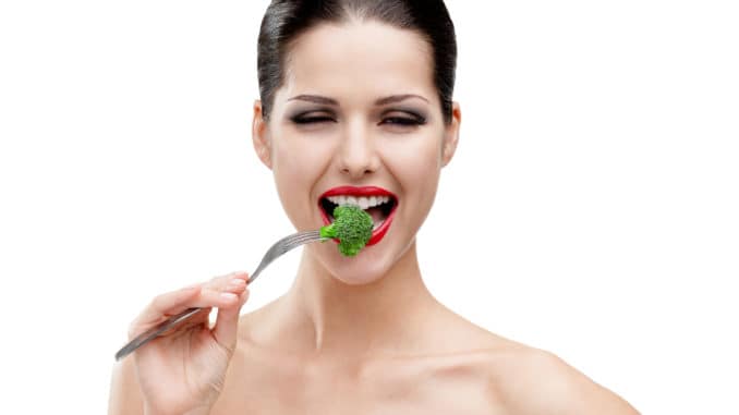 Woman with red lipstick eating broccoli on the stainless fork, isolated on white. Fresh and healthy dieting food