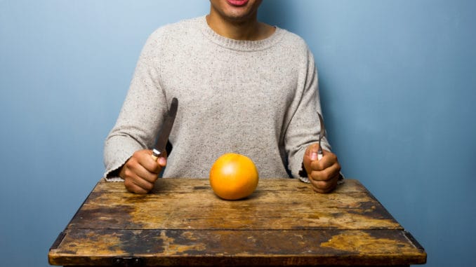 Healthy young man having a grapefruit for dinner at old table