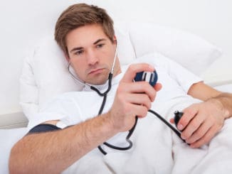 Man Lying On Bed Checking His Own Blood Pressure