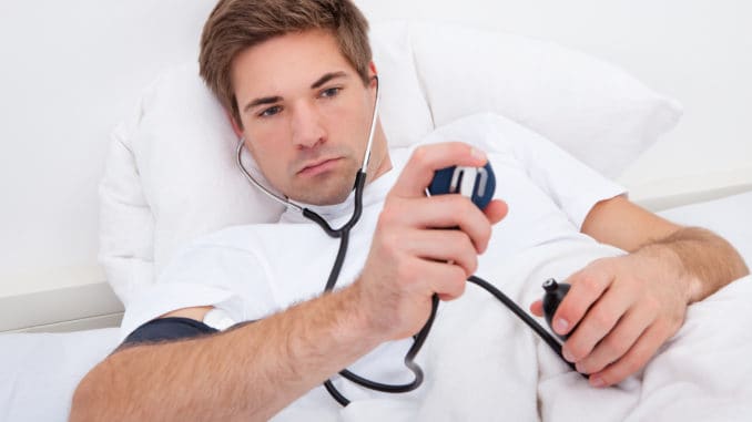 Man Lying On Bed Checking His Own Blood Pressure