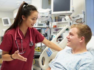 Young Male Patient Talking To Female Nurse In Emergency Room Wearing Scrubs Looking At Each Other