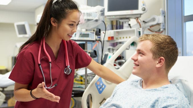 Young Male Patient Talking To Female Nurse In Emergency Room Young Male Patient Talking To Female Nurse In Emergency Room Wearing Scrubs Looking At Each Other