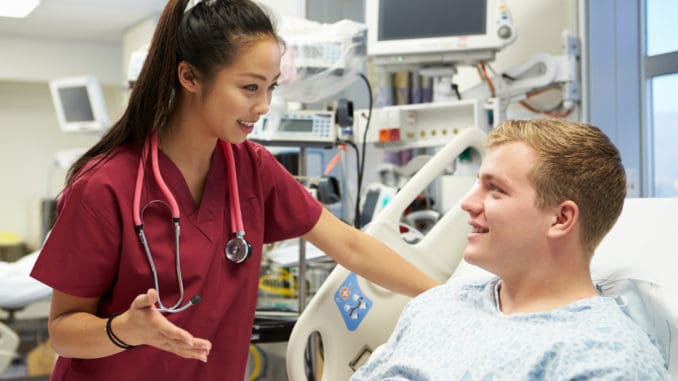 Young Male Patient Talking To Female Nurse In Emergency Room Wearing Scrubs Looking At Each Other