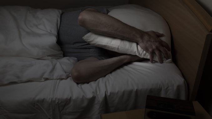 Mature man, with pillow covering entire face, cannot sleep at night from insomnia