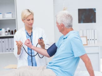 Female doctor checking senior mans blood pressure in clinic