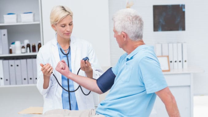 Female doctor checking senior mans blood pressure in clinic