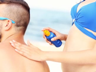 A picture of a women applying sunscreen on the back of her men at the beach