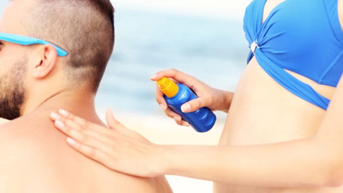 A picture of a women applying sunscreen on the back of her men at the beach