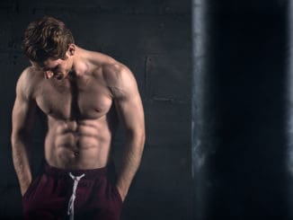 Athletic man with naked torso near concrete wall in the studio looking down