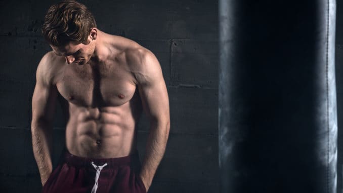 Athletic man with naked torso near concrete wall in the studio looking down