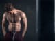 Athletic man with naked torso near concrete wall in the studio looking down