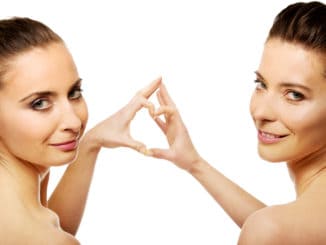 Two beautiful women making heart with fingers.