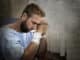 Young injured man in hospital room sitting alone in pain looking negative and worried for his bad health condition sitting on chair suffering depression on a sad lonely background