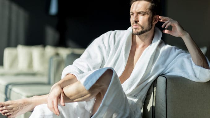 Young, handsome man in the morning thinking while sitting in a hotel room in a robe