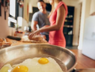 Fried eggs in a pan with couple standing in background are out of focus in domestic kitchen