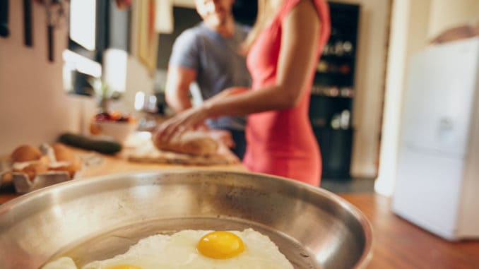 Fried eggs in a pan with couple standing in background are out of focus in domestic kitchen
