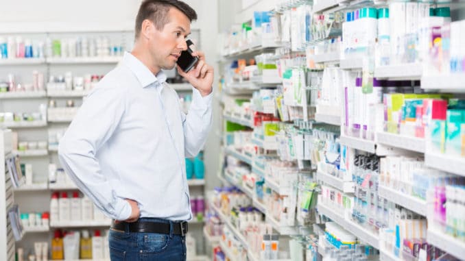 Confused mid adult man using mobile phone while looking at products in pharmacy