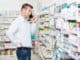 Confused mid adult man using mobile phone while looking at products in pharmacy