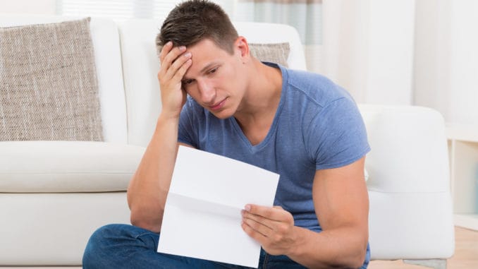 Shocked Young Man Looking At Paper In Living Room