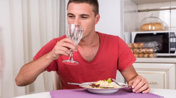 Young Man Taking Sip of Water During Dinner of Home Cooked Pasta While Seated at Dining Table in Quaint Kitchen