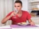Young Man Taking Sip of Water During Dinner of Home Cooked Pasta While Seated at Dining Table in Quaint Kitchen