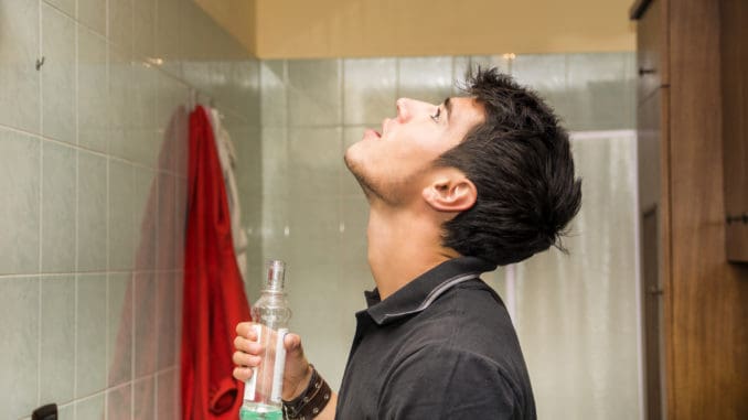 Handsome young man using mouthwash to clean his teeth and mouth