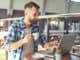 Young adult man drinking coffee and using laptop in cafe