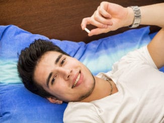 Young attractive man in bed taking one medicine tablet or pill