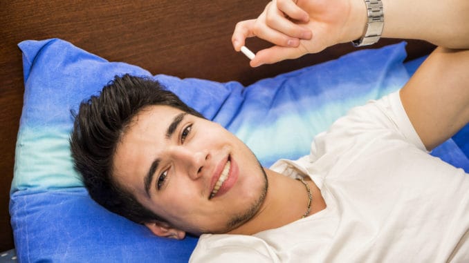 Young attractive man in bed taking one medicine tablet or pill