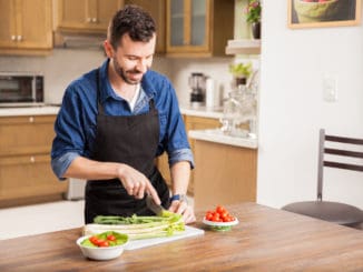 Good looking man in an apron cutting some vegetables to make himself a salad at home