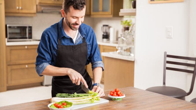 Good looking man in an apron cutting some vegetables to make himself a salad at home