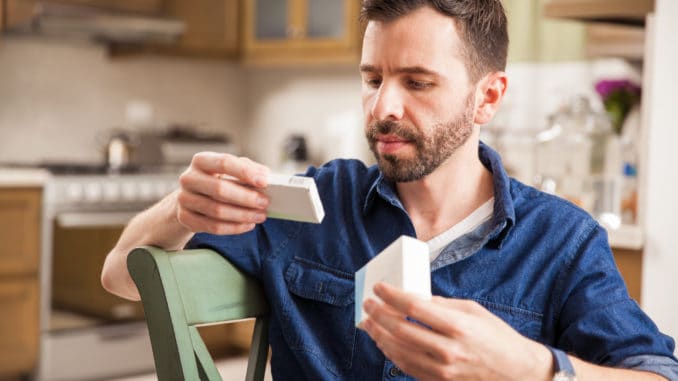 Attractive man with a beard holding a couple of boxes of medicine and comparing each other at home