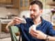 Attractive man with a beard holding a couple of boxes of medicine and comparing each other at home