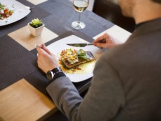 Young man eating grilled salmon with sauce and herbs served at restaurant