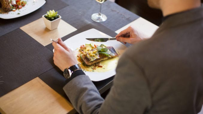 Young man eating grilled salmon with sauce and herbs served at restaurant