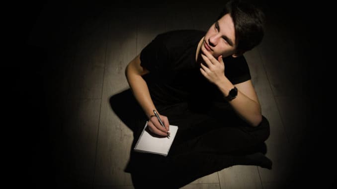 Teenager young man thinking and writing on notebook on black background