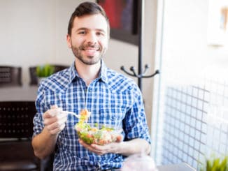 Portrait of a young Hispanic man eating a salad at a restaurant and smiling