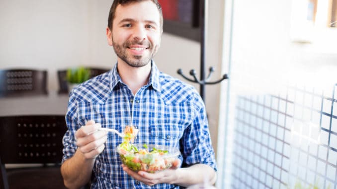 Portrait of a young Hispanic man eating a salad at a restaurant and smiling