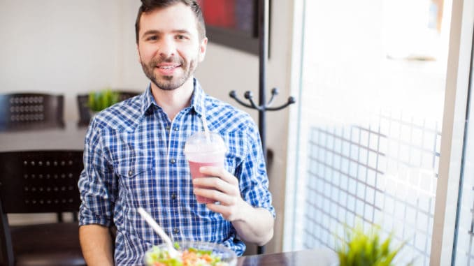 Portrait of a young Latin man eating some healthy food and enjoying a smoothie alone at a restaurant