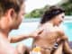 Man applying sunscreen on back of her woman near pool on a sunny day