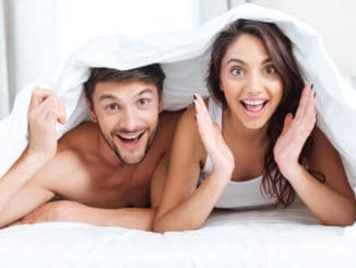 Happy smiling couple lying in bed covered with blanket at home