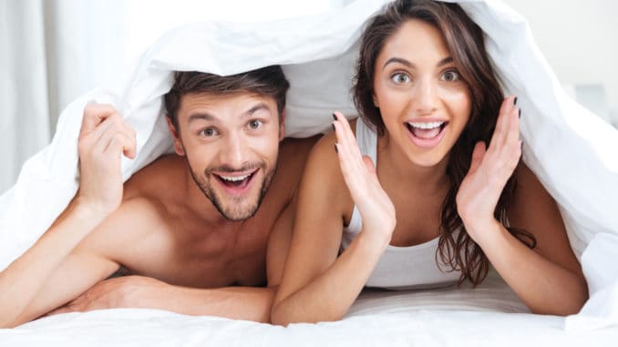 Happy smiling couple lying in bed covered with blanket at home