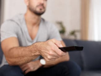 Man chaning TV channel by remote control at home