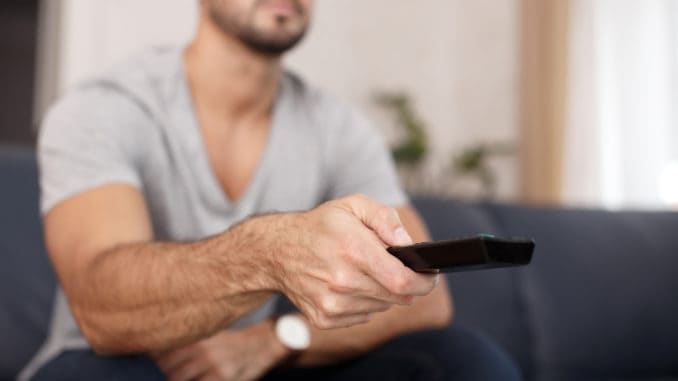 Man chaning TV channel by remote control at home