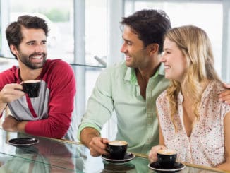 Smiling women and two men having cup of coffee in cafe