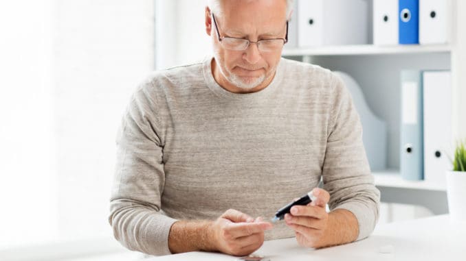 Medicine, age, diabetes, health care and old people concept - senior man with glucometer checking blood sugar level at home