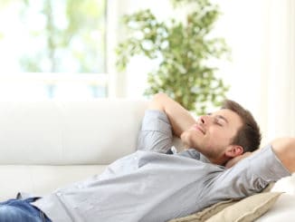 Relaxed man resting lying on a couch with the hands on the head at home