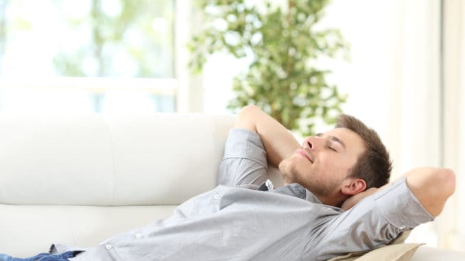 Relaxed man resting on a couch at home Relaxed man resting lying on a couch with the hands on the head at home