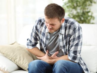 Man suffering stomach ache sitting on a couch in the living room at home