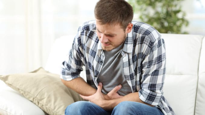 dreamstime_m_83873628 Man suffering stomach ache sitting on a couch in the living room at home